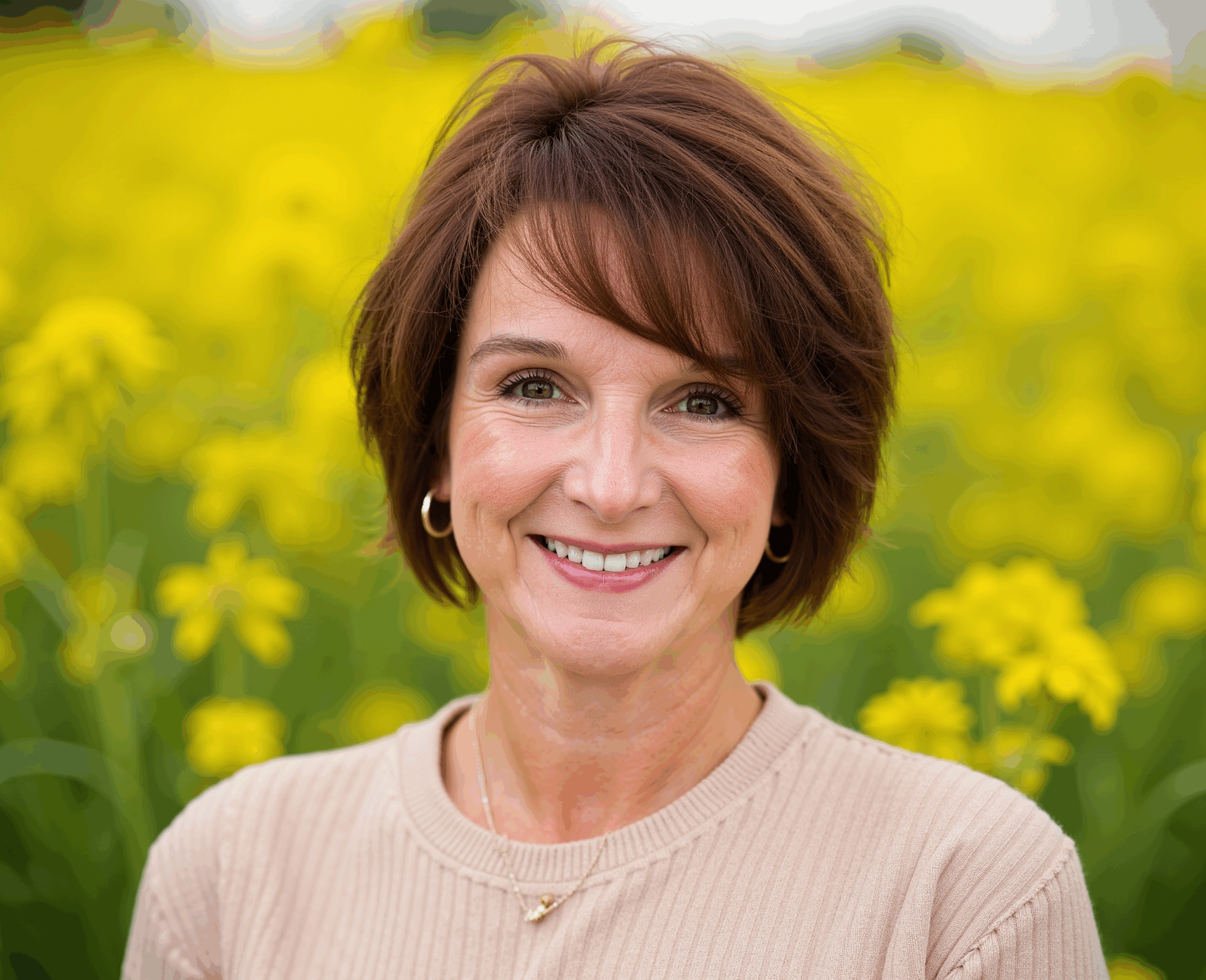 Smiling woman in a beige top standing in a yellow flower field.