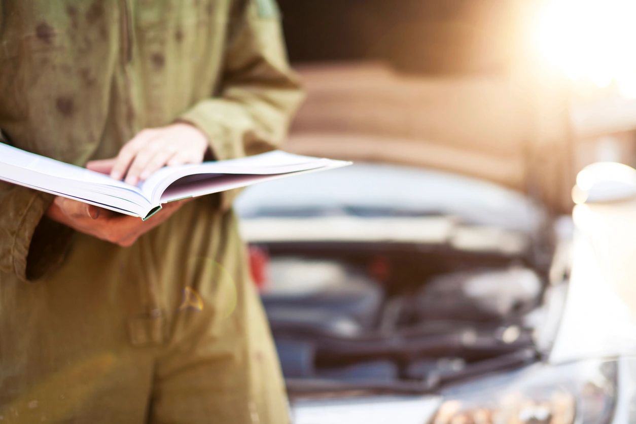 Person reading a manual near an open car hood.