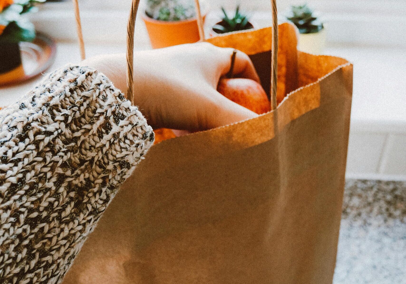 Person placing fresh carrots into a brown paper grocery bag.
