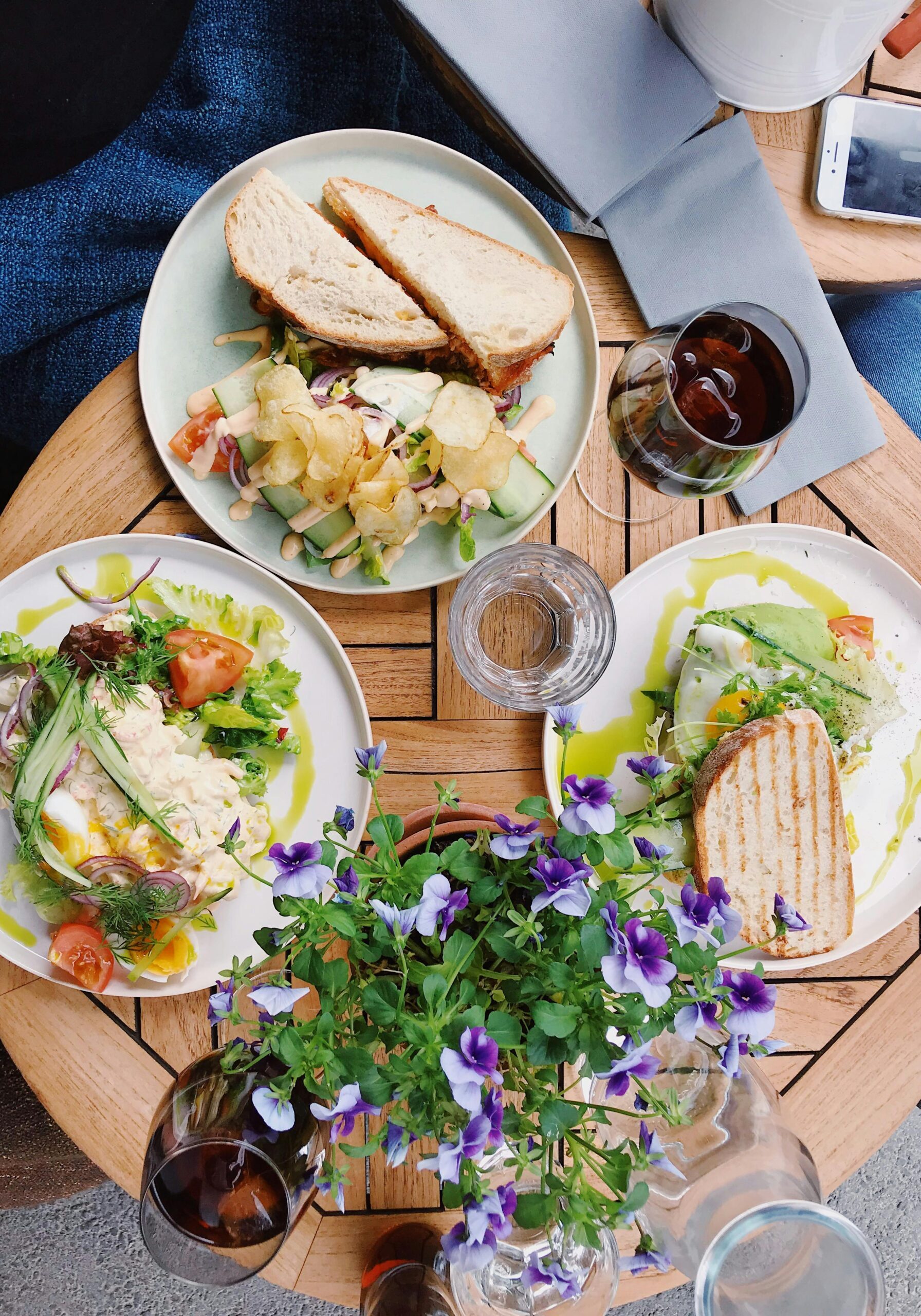 A table with three plates of sandwiches and salads, a glass of juice, and a coffee cup.